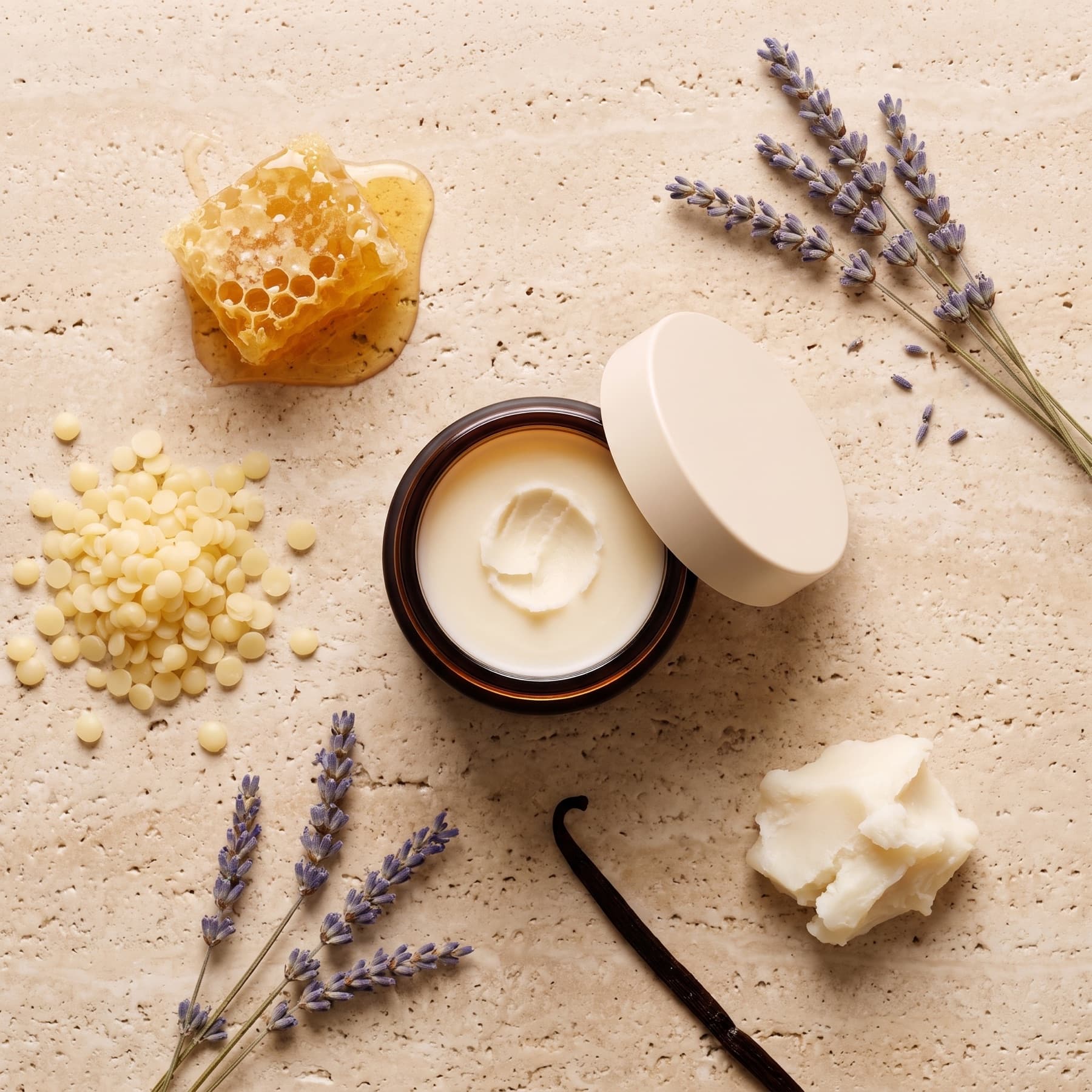 Honeycomb, beeswax pellets, lavender, vanilla bean and raw tallow around an open jar of balm